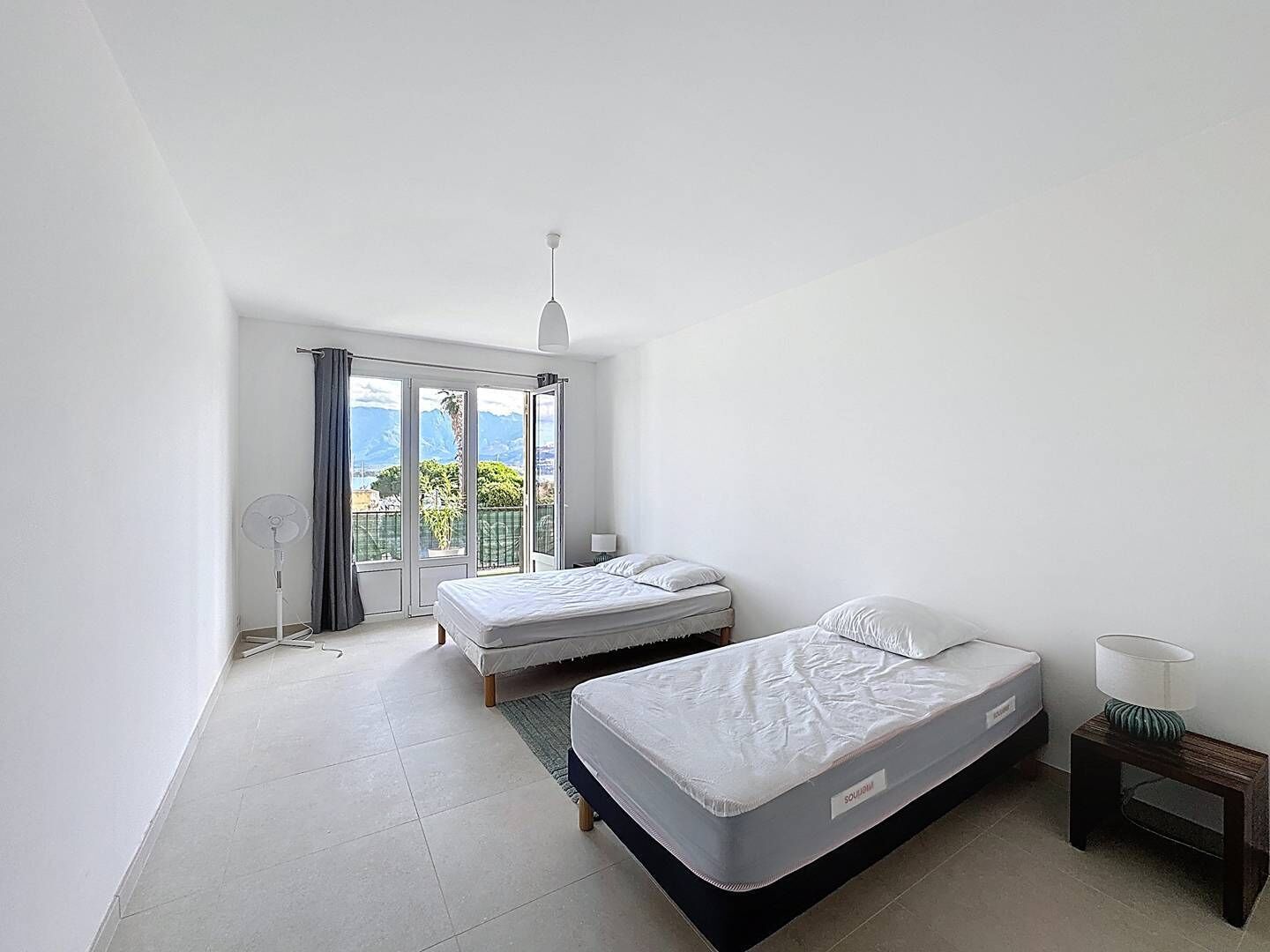 Un dormitorio con dos camas, un ventanal con vistas y un ventilador de techo.