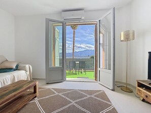 A modern bedroom with a large sliding glass door leading to a balcony with a view of mountains and a palm tree. - Calvi à pied : terrasse vue mer, 2 chambres, parking privé (CALVI)