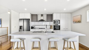 Una cocina moderna con armarios blancos, electrodomésticos de acero inoxidable y una isla central con taburetes de bar.