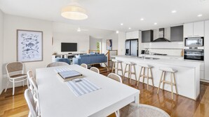 Una cocina moderna con armarios blancos, una isla central y un comedor con mesa y sillas blancas.