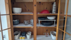 A wooden cabinet with shelves containing bowls, plates, glasses, and a red colander. - Sunny Private Floor in Stylish Home w Parking (Kingston)