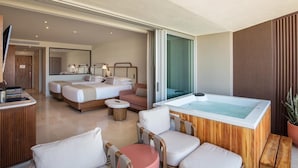 A modern hotel room with a large bed, a sitting area with a coffee table, a hot tub, and a wooden panel wall. - Corazon Cabo, Infinty Two Queen Sunset View Hot Tub, Spend New Year's in Cabo (Cabo San Lucas)
