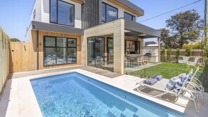 Een modern huis met twee verdiepingen, een zwembad, terras en een verzorgd gazon.