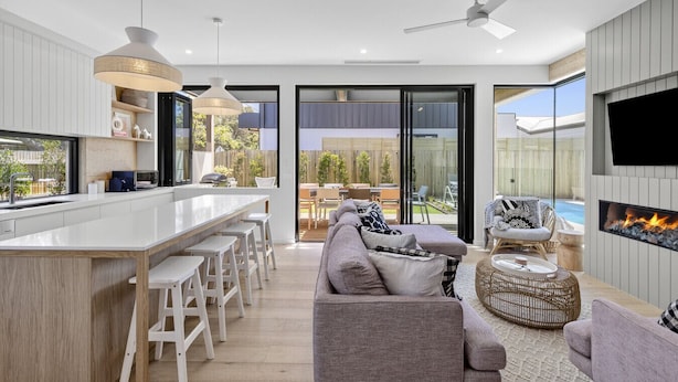 Een moderne keuken met een centraal eiland, barkrukken en een eethoek. Er is een zithoek met een bank en een open haard.