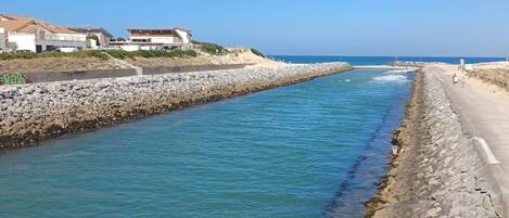 A coastal walkway with a rocky barrier, clear blue water, and buildings in the background.