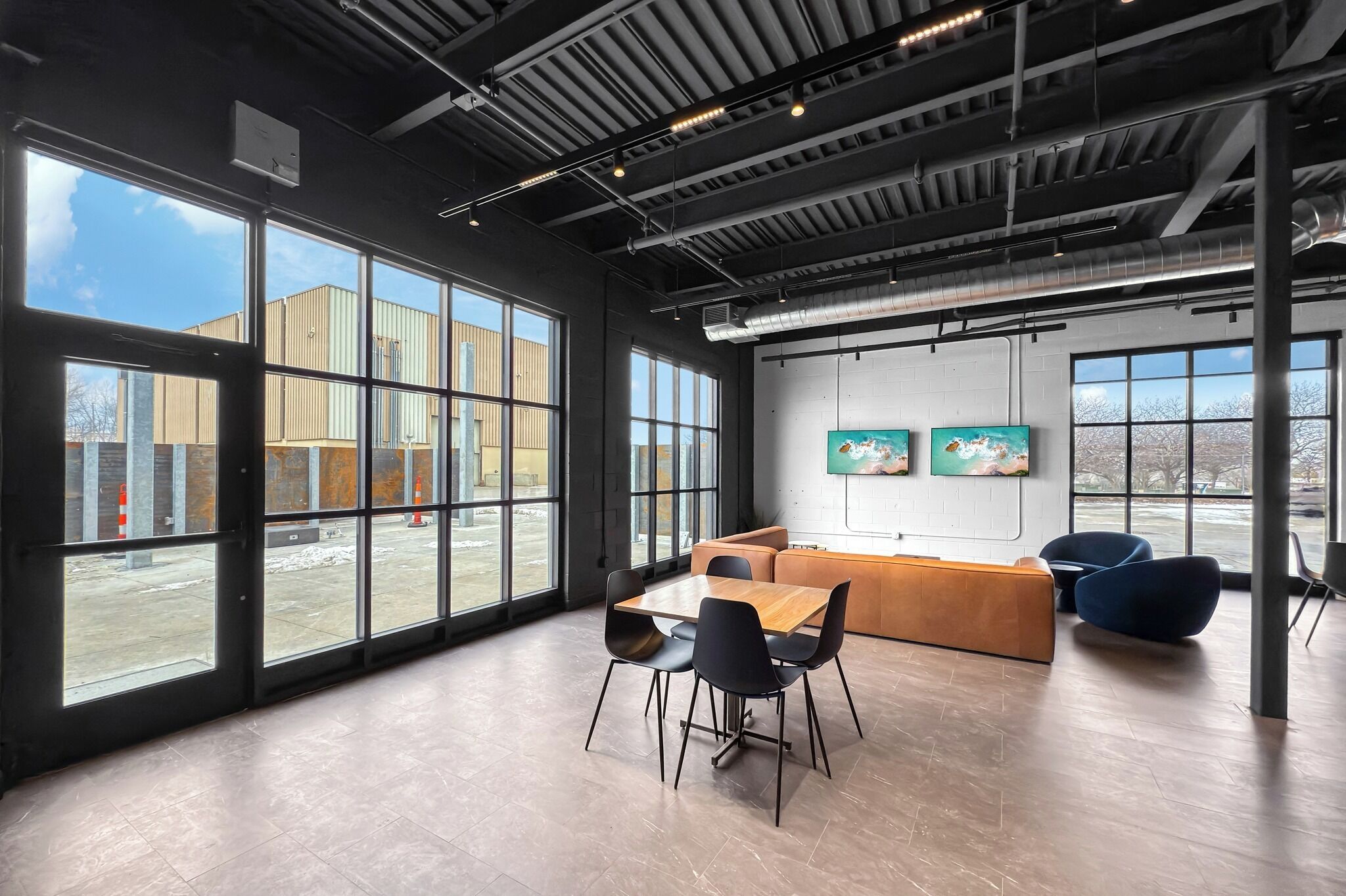 Una habitación amplia con ventanas grandes, una mesa de madera con sillas, un sofá y un televisor montado en la pared.