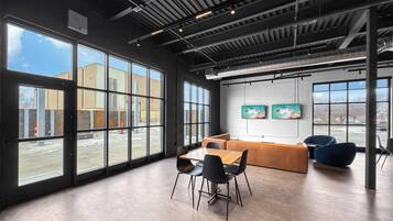 Una habitación amplia con ventanas grandes, una mesa de madera con sillas, un sofá y un televisor montado en la pared.