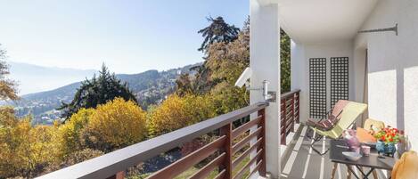 Uma varanda com grade de madeira, uma mesa com cadeiras e vista para um vale com árvores de outono.