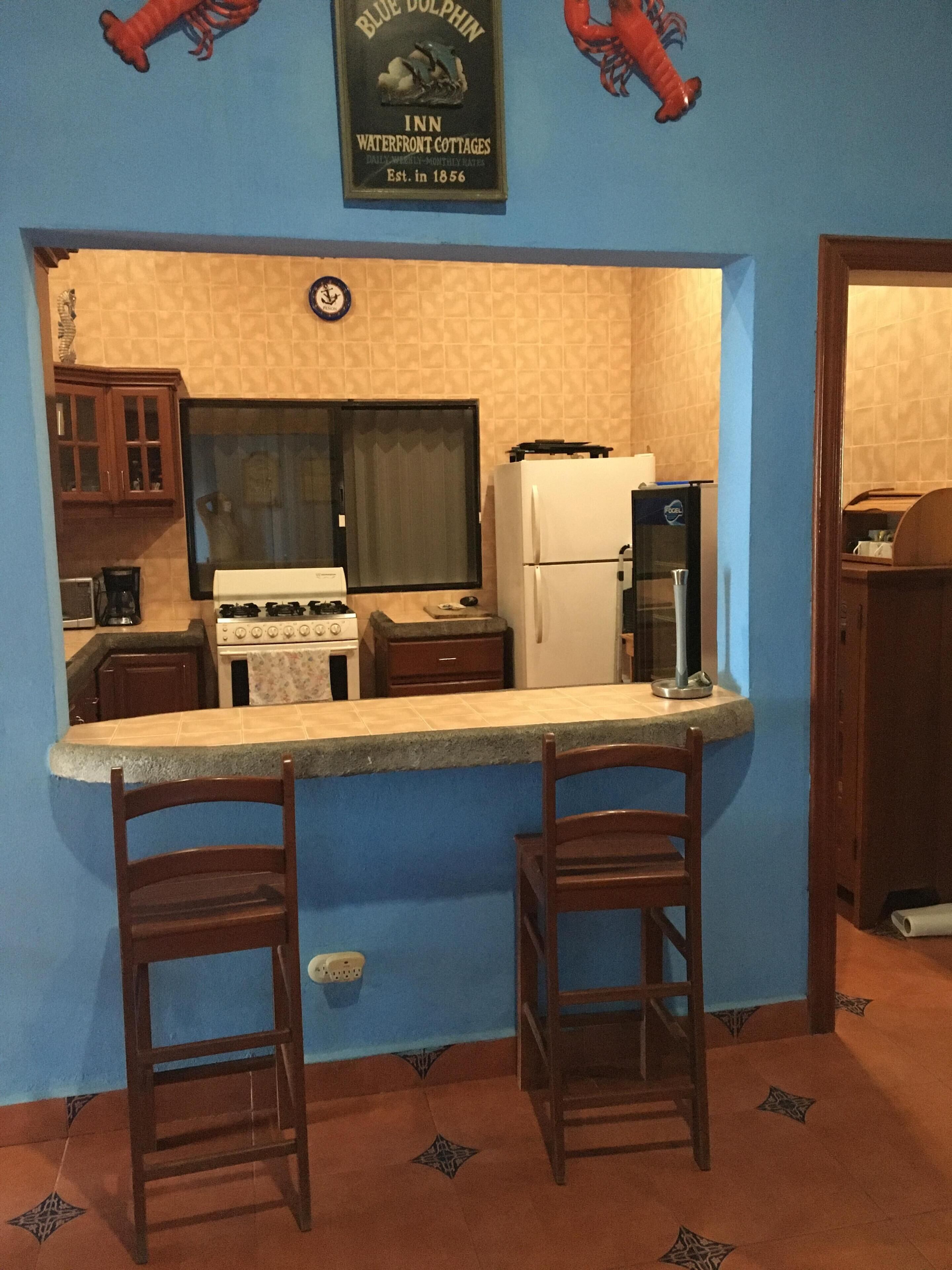 A compact kitchen with a stove, refrigerator, and bar stools.