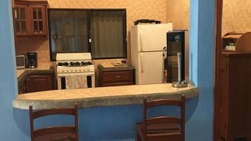 A compact kitchen with a stove, refrigerator, and bar stools.