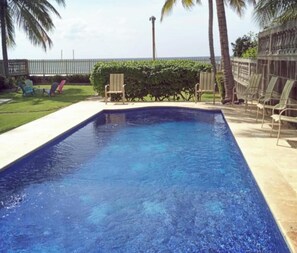 Una piscina rectangular con superficie de agua azul cristalina, rodeada por un solárium con baldosas.