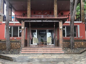 Un edificio con fachada roja, pilares de piedra y un balcón con sillas y una mesa.