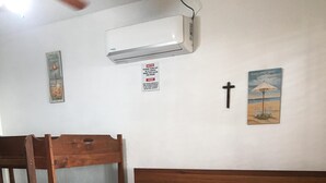 A bedroom with a bunk bed, a wooden headboard, a bed with a patterned bedspread, a wall-mounted air conditioner, and a small cross decoration.
