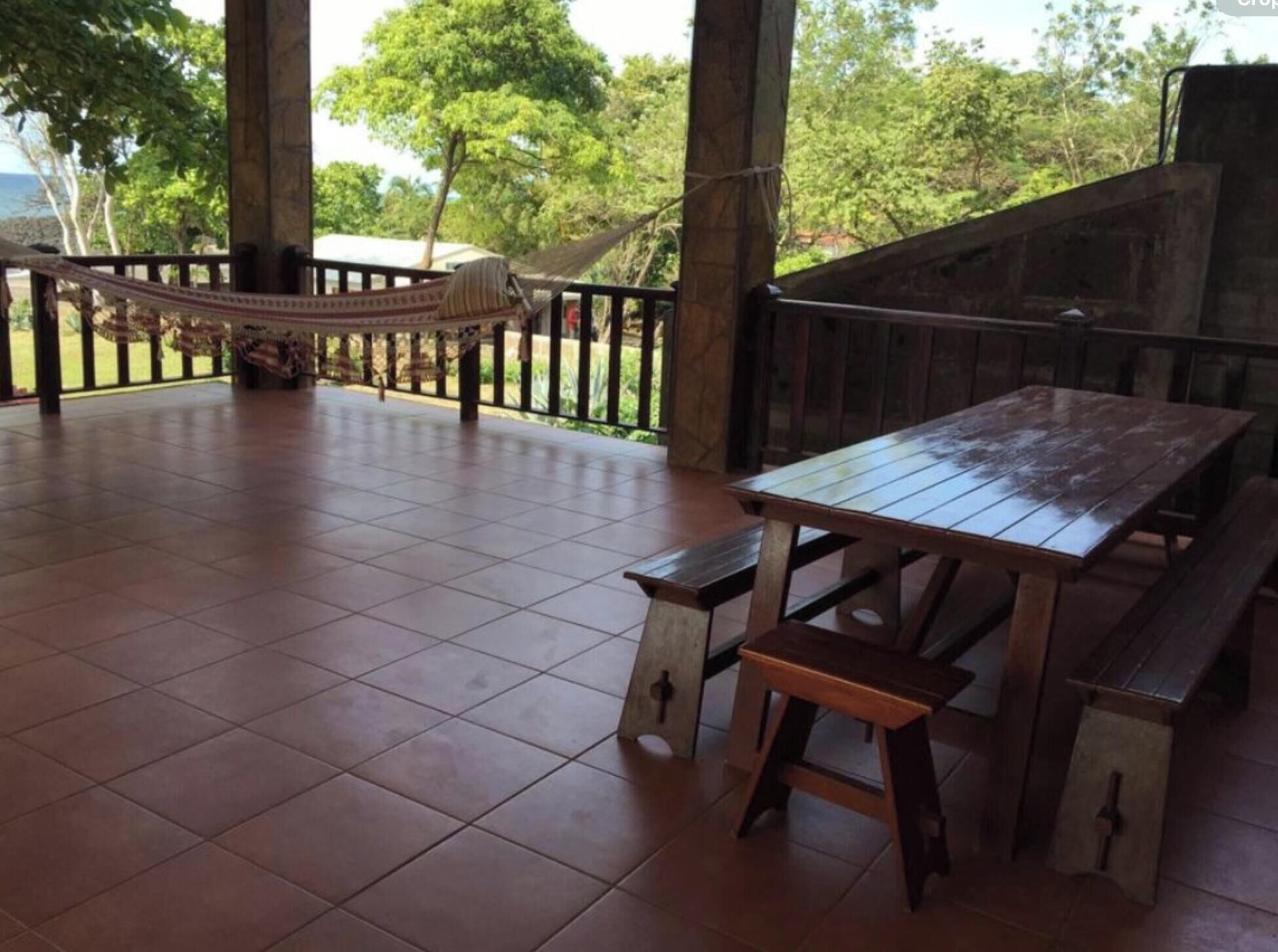 Une terrasse extérieure couverte, avec une table et des bancs en bois, entourée d’un sol carrelé et agrémentée d’un hamac.