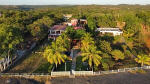 An aerial view of a property with multiple buildings, surrounded by lush greenery and palm trees.