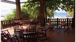 A covered outdoor seating area with wooden furniture and a view of the ocean.