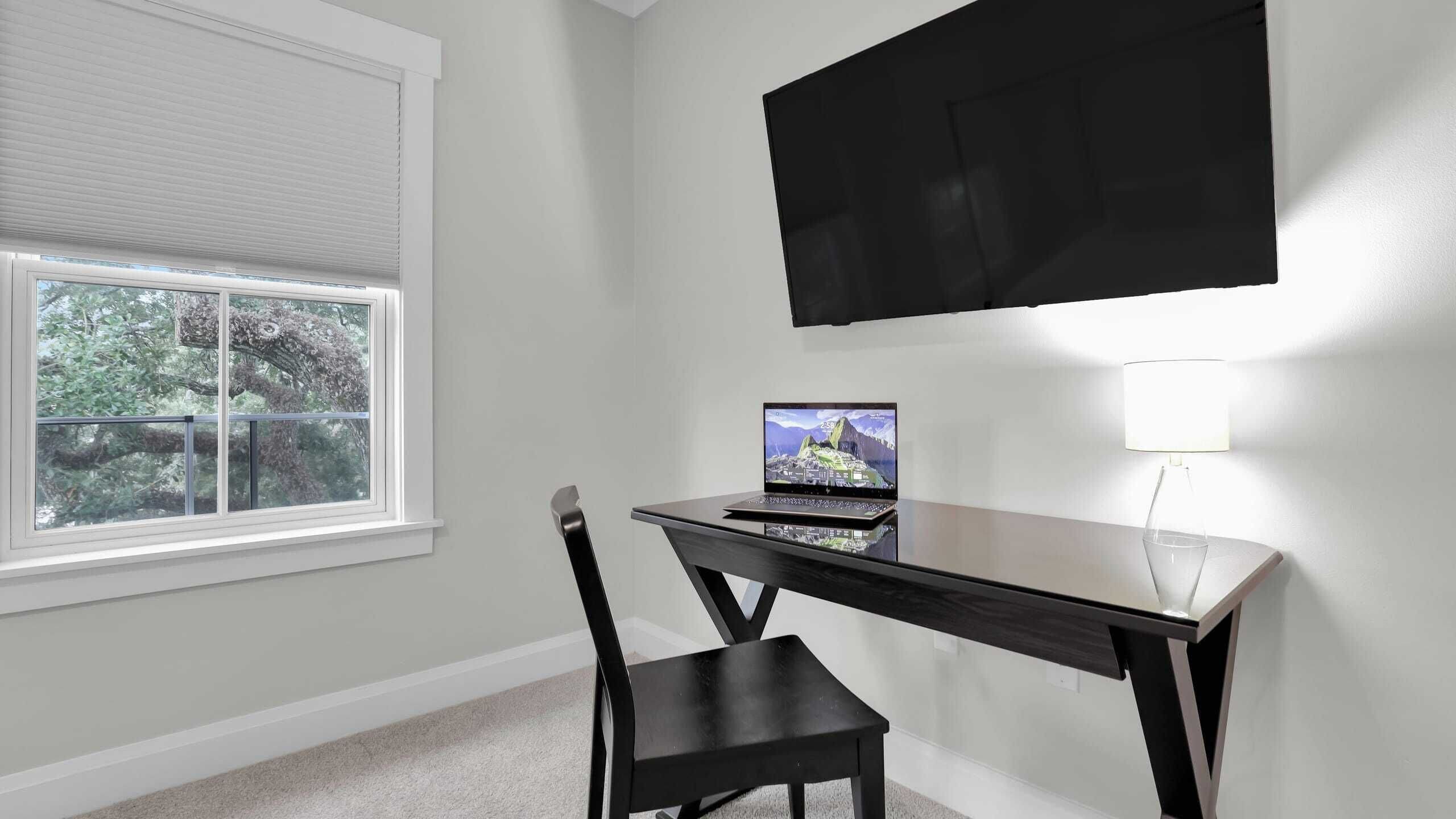 A room with a desk, chair, and a TV mounted on the wall.
