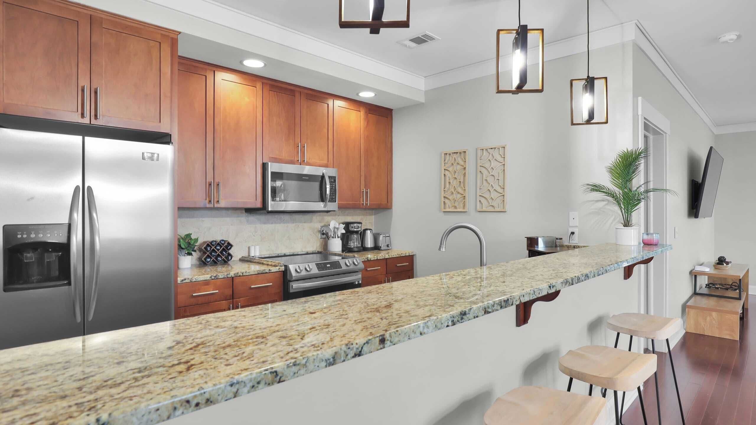 A modern kitchen with granite countertops, stainless steel appliances, wooden cabinets, and pendant lighting.