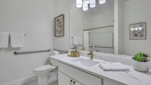 A modern bathroom with a white sink, gold faucet, and a large mirror. There are two towels on the wall and a handrail. - The Juliette by AvantStay (Savannah)