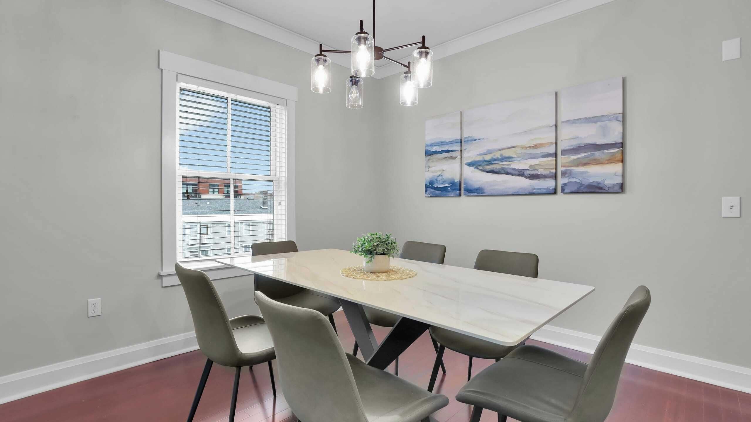 A dining area with a rectangular table, six chairs, a potted plant, and a modern chandelier.