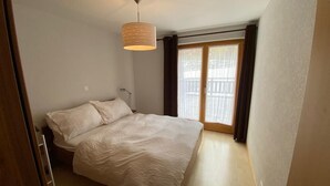 A bedroom with a bed, a hanging light fixture, a window with curtains, and a door. - Very comfortable 3-room apartment for 3-4 persons : Living room - kitchen with dishwasher, filter co (Grimentz)