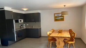 A modern kitchen with dark cabinets, a microwave, and a coffee maker. There is a wooden dining table with chairs and a red chair in the foreground. - Very comfortable 3-room apartment for 3-4 persons : Living room - kitchen with dishwasher, filter co (Grimentz)