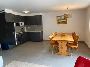 A modern kitchen with dark cabinets, a microwave, and a coffee maker. There is a wooden dining table with chairs and a red chair in the foreground. - Very comfortable 3-room apartment for 3-4 persons : Living room - kitchen with dishwasher, filter co (Grimentz)