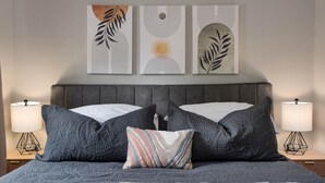 A bed with a grey headboard, two bedside lamps, and three wall art pieces above. - Cozy Ranch King Bed & Pet Friendly - Fenced Yard (Gahanna)