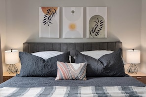A bed with a grey headboard, two bedside lamps, and three wall art pieces above. - Cozy Ranch King Bed & Pet Friendly - Fenced Yard (Gahanna)