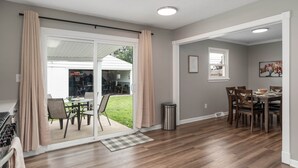 A spacious living area with a sliding glass door leading to a patio, a dining table with chairs, and a piano. - Cozy Ranch King Bed & Pet Friendly - Fenced Yard (Gahanna)