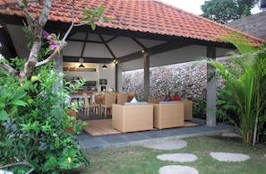 An outdoor patio area with wicker furniture, a stone wall, and a tiled roof. - Carang Sari Sukawati 3-bedroom villa river side with private swimming pool (Sukawati Gianyar)