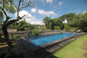 Ein rechteckiger Swimmingpool mit Steinbord, umgeben von einer Rasenfläche und Bäumen.