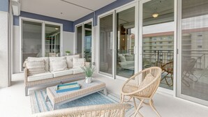 A balcony with a white sofa, wicker chairs, and a blue rug. - Luxurious 4BR Ocean‑View Retreat with Soaking Tub & Pool Access 🌊 (Cocoa Beach)