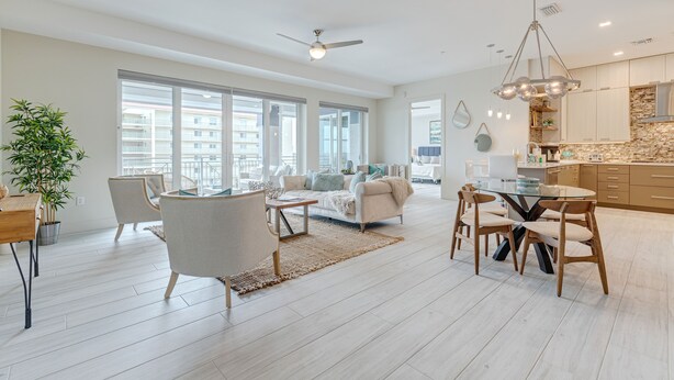 A spacious living area with a sofa, dining table, and chairs, large windows, and a kitchen area with modern appliances. - Luxurious 4BR Ocean‑View Retreat with Soaking Tub & Pool Access 🌊 (Cocoa Beach)