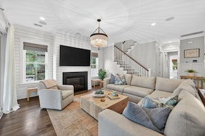 A spacious living room with a fireplace, a large sofa, a coffee table, and a staircase leading to another level. - Spacious 6-bedroom home on IOP! Close to island amenities and private pool! (Isle Of Palms)