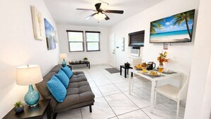 A modern living room with a sofa, coffee table, and a dining area with a table set for breakfast. - Hollywood Beach 1BR | 30 Sec to Sand + Kitchen (Hollywood)
