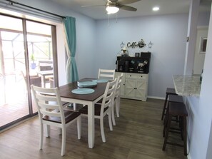 A dining area with a table set for four, white chairs, a ceiling fan, and a coffee station with a sign.