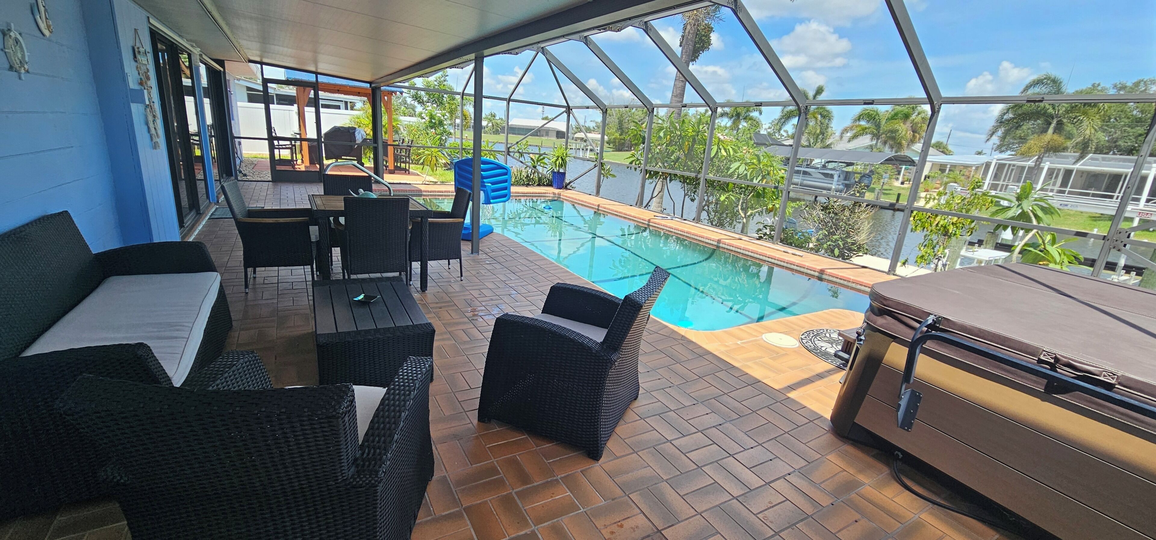 A covered outdoor area with a pool, wicker furniture, and a grill.