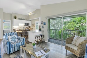A spacious living area with a kitchen, a balcony with a view of greenery, and a dining area with wicker furniture. - Walking distance to Siesta Key Beach & Village w/Heated Pool & Outdoor Dining (Siesta Key)