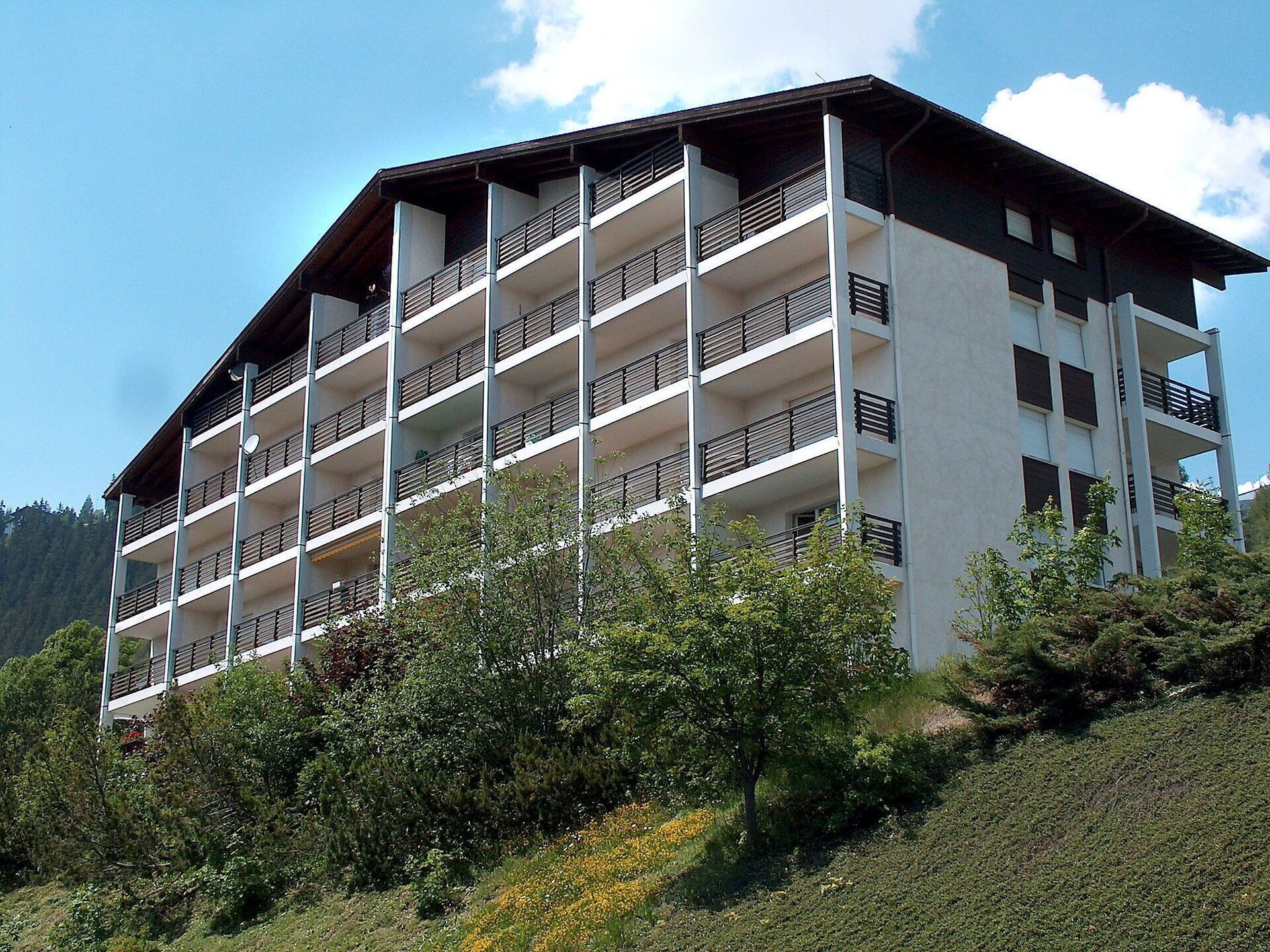 Un hotel de varios pisos con balcones, rodeado de vegetación y colinas.