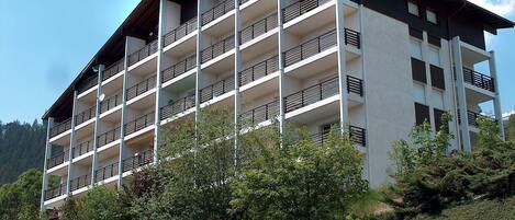 Un hotel de varios pisos con balcones, rodeado de vegetación y colinas.