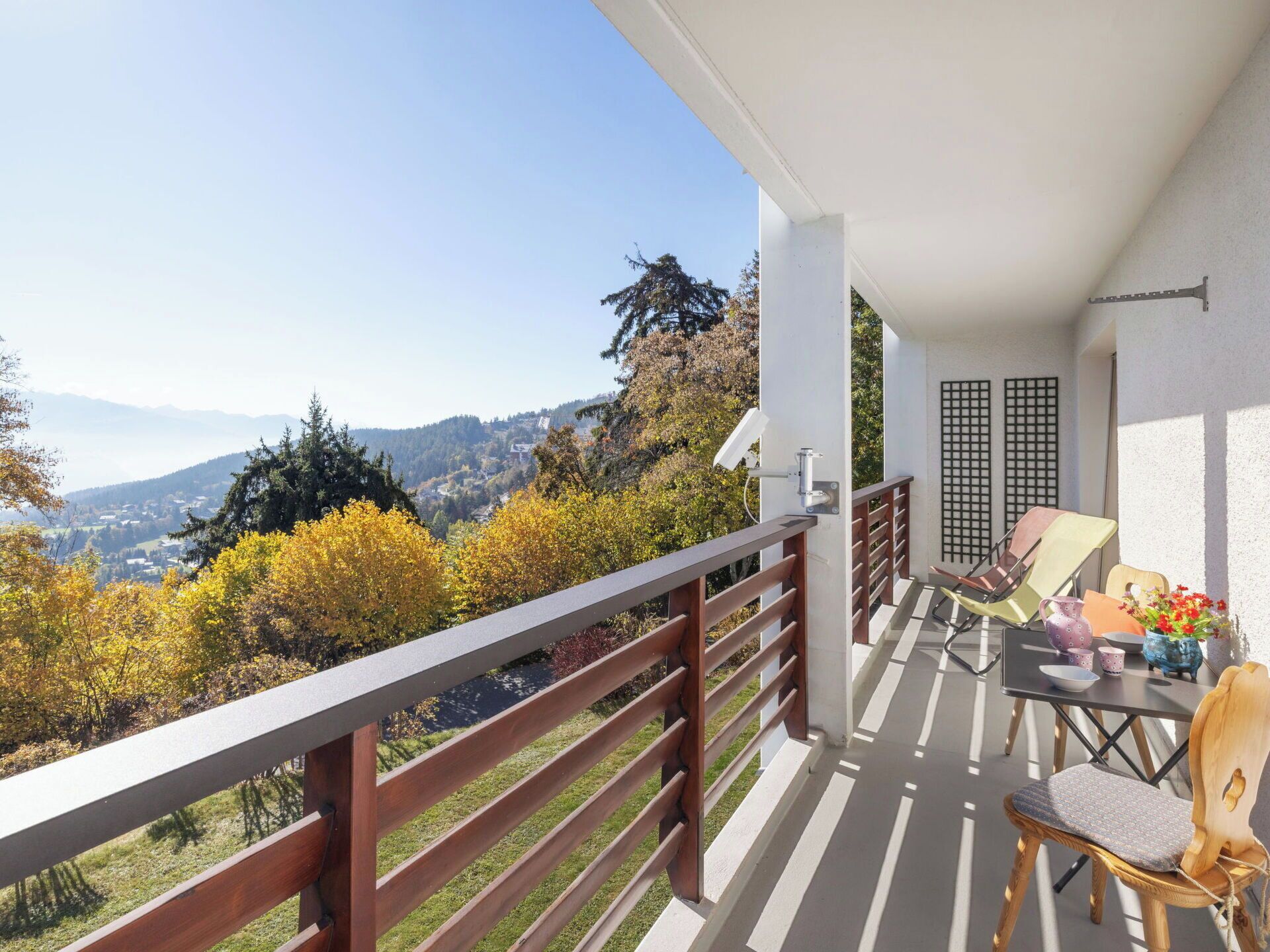 Een balkon met uitzicht op een bergachtig landschap, een tafel met stoelen, en een bijzettafeltje met decoratieve objecten.