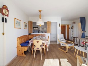 Ein gemütliches Wohnzimmer mit einer Holzbank, einem Esstisch und einer Küche im Hintergrund.