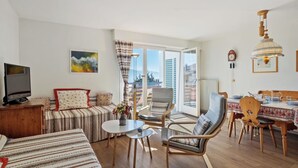 A modern living room with a sofa, chairs, a dining table, and a TV. - Cosy apartment for 4 people with WIFI, TV, balcony and panoramic view (Bluche)