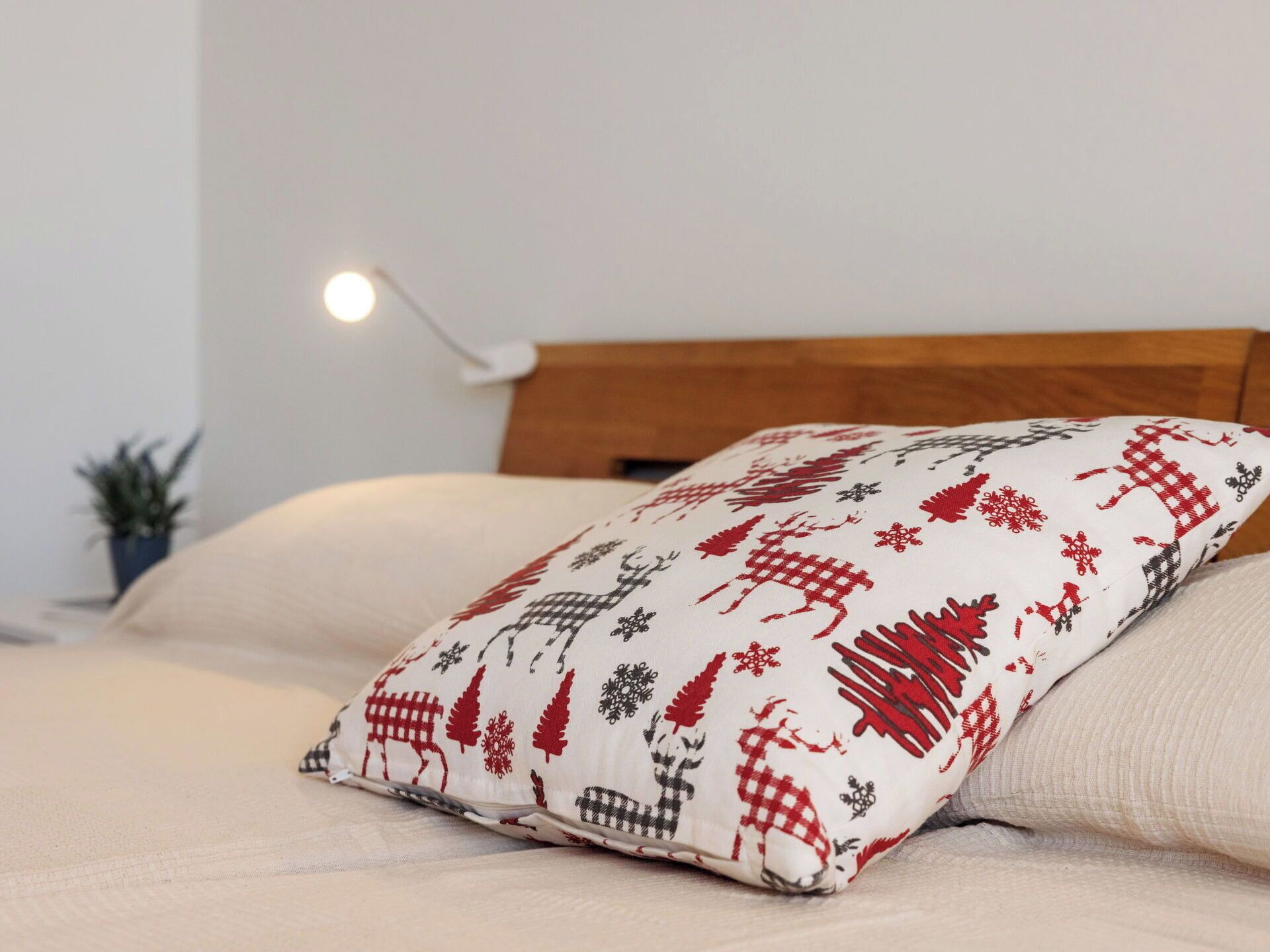 Una cama con un cojín de diseño rojo y blanco, cabecera de madera y una lámpara de noche.