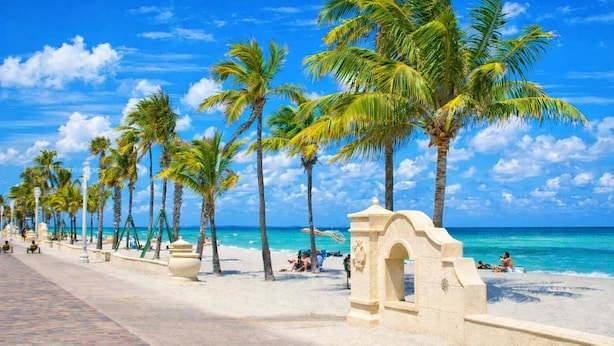 Een strand met palmbomen, een verhard voetpad en een stenen gebouw.