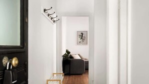 A hallway with a black door, a white wall with a black and white artwork, a grey sofa, and a small plant. - Charming 2Bed Home Near Cafés & Racecourse (Hamilton)