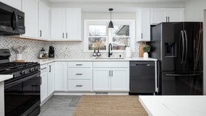 A modern kitchen with white cabinets, a black refrigerator, a stove, and a sink. - Clean & Cozy 4BR Retreat, Hot Tub, 1 Mile to DTP (Plymouth)