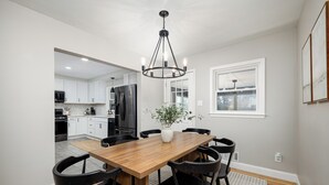 A dining area with a wooden table and black chairs, a chandelier, and a potted plant. - Clean & Cozy 4BR Retreat, Hot Tub, 1 Mile to DTP (Plymouth)