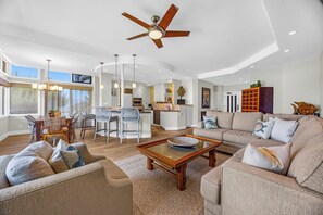 A spacious living area with a dining table, sofas, a coffee table, a ceiling fan, and a kitchen in the background. - Kapalua Ridge | Ocean View 5 BR, Sleeps 18 | Car Incl. w/ 6+ Nights | KRV ML-2513 by KBM (Lahaina)